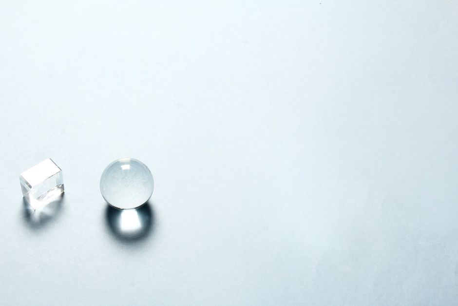 Minimalist composition with a transparent crystal sphere and cube casting shadows on a light background.