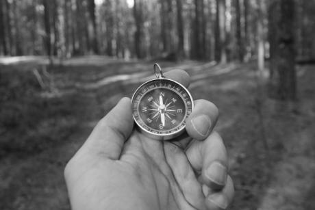 A black and white photo of a man holding a compass during a forest exploration, symbolizing navigation.