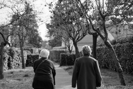 Black and white photo of two senior adults walking through a park during the day.