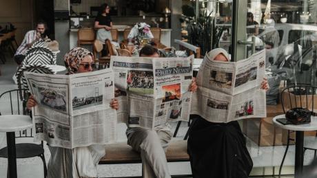 Three adults reading newspapers in a modern Ankara café, enjoying leisure time.