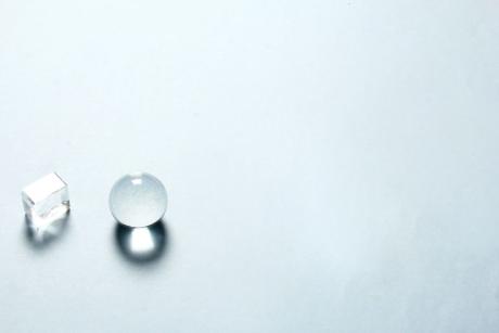Minimalist composition with a transparent crystal sphere and cube casting shadows on a light background.