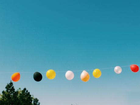 A row of vibrant balloons hanging against a clear blue sky in summer.