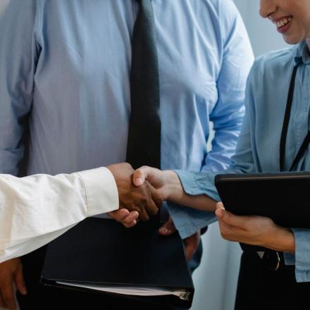 Crop unrecognizable diverse partners in formal clothes with documents shaking hands during business meeting in office