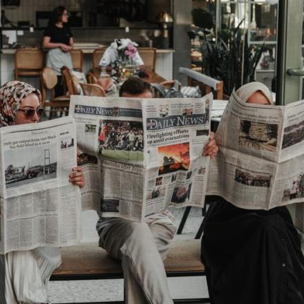 Three adults reading newspapers in a modern Ankara café, enjoying leisure time.