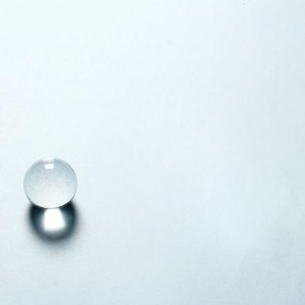Minimalist composition with a transparent crystal sphere and cube casting shadows on a light background.