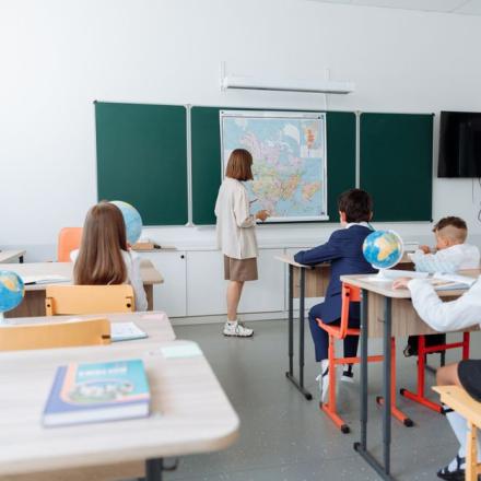 Students engaged in a geography lesson, focusing on a wall map in a classroom with globes and study materials.
