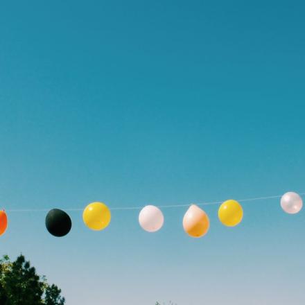 A row of vibrant balloons hanging against a clear blue sky in summer.