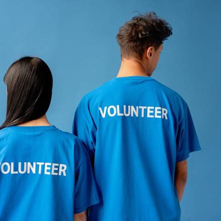 Two people wearing blue volunteer shirts standing against a blue background.
