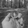 A black and white photo of a man holding a compass during a forest exploration, symbolizing navigation.
