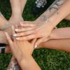 A group of people's hands with tattoos and colorful nails symbolizing unity on grass.