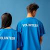 Two people wearing blue volunteer shirts standing against a blue background.